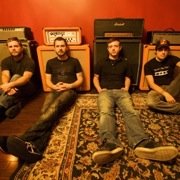 Thumbnail: With Friends Like These band members sitting against guitar amps.