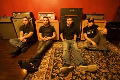 With Friends Like These band members sitting against guitar amps.